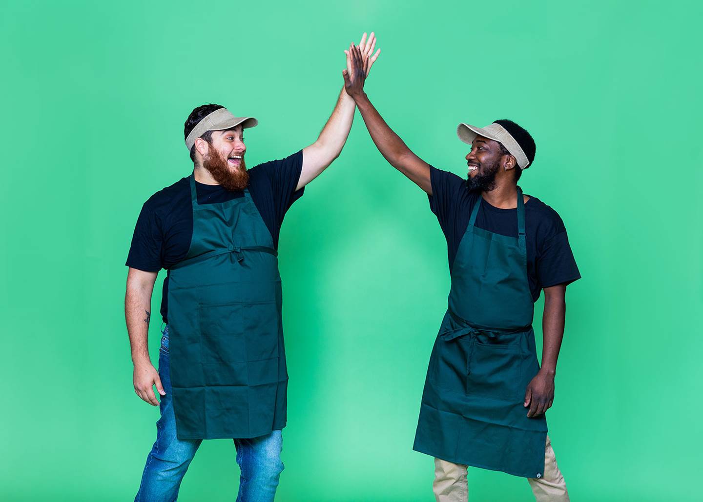 2 men in their work aprons giving each other a high five in front of a green background.